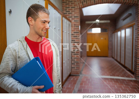 Teenage boy standing in school hallway by lockers holding blue binder wearing hoodie, copy space Teenage boy standing in school hallway by lockers holding blue binder wearing hoodie, copy space 135362750