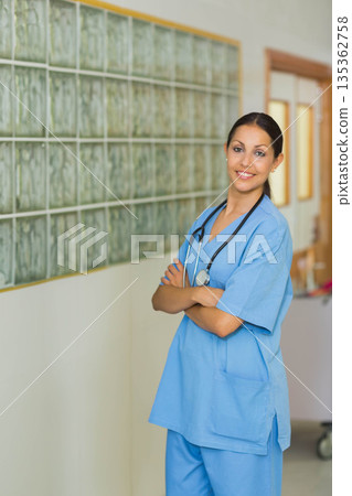 Female nurse posing in scrubs with stethoscope in hospital hallway by glass block wall, copy space Female nurse posing in scrubs with stethoscope in hospital hallway by glass block wall, copy space 135362758