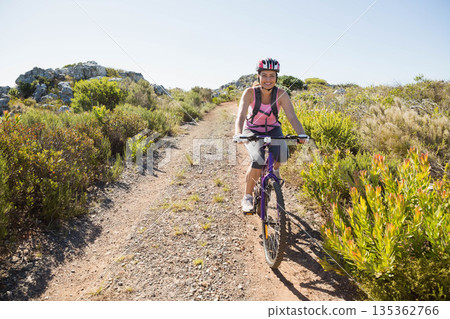 Woman riding mountain bike in athletic gear on rocky trail in scrubland wearing helmet and backpack Woman riding mountain bike in athletic gear on rocky trail in scrubland wearing helmet and backpack 135362766
