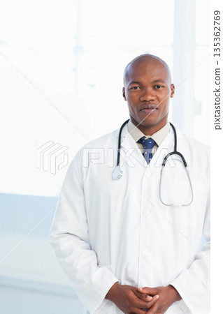 African American male doctor standing in exam room wearing white lab coat, stethoscope, copy space 135362769