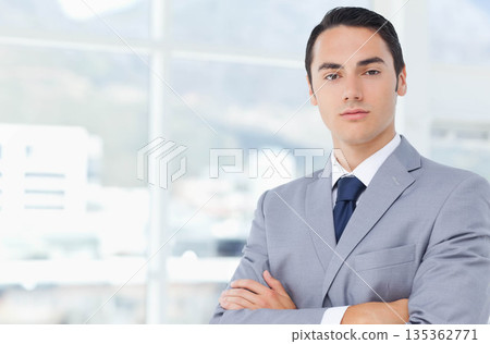 Man in early thirties wearing grey suit standing in office near tall glass windows, copy space 135362771