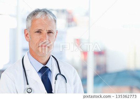 Male doctor standing in clinic reception area wearing lab coat and stethoscope, copy space 135362773
