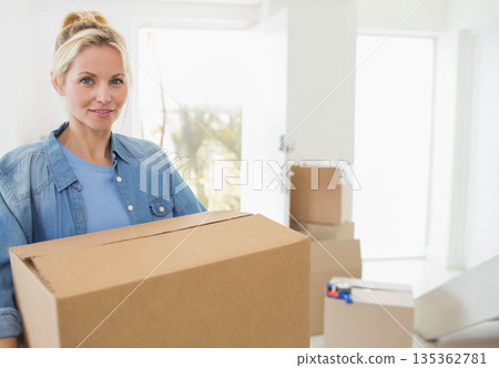 Woman holding cardboard box in entryway with moving boxes by open front door, copy space 135362781