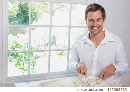 Middle-aged man cutting food on plate at bright dining table by window, glass beverages, copy space Middle-aged man cutting food on plate at bright dining table by window, glass beverages, copy space 135362783