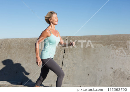 Senior woman jogging on walkway by concrete sea wall in sportswear with athletic shoes, copy space Senior woman jogging on walkway by concrete sea wall in sportswear with athletic shoes, copy space 135362790