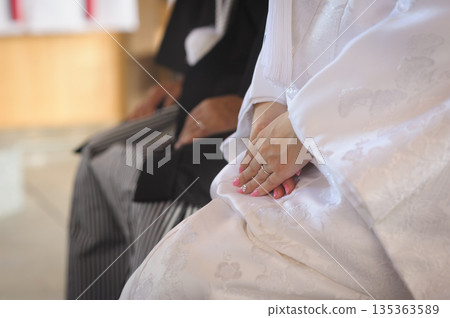 Bride and groom during a Shinto ceremony. The bride's hands and wedding rings gently overlap. Japanese wedding bridal advertising material. Bride and groom during a Shinto ceremony. The bride's hands and wedding rings gently overlap. Japanese wedding bridal advertising material. 135363589