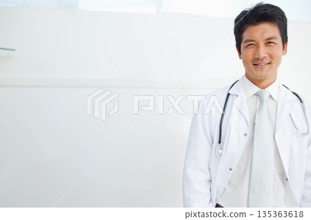 Mid-adult Japanese doctor standing at clinic door wearing white coat and stethoscope, copy space 135363618