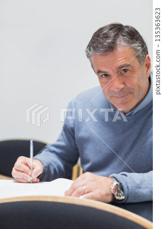 Middle-aged man writing in open notebook on wooden table in meeting room using silver pen 135363623