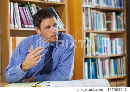 Mid adult man sitting at wooden library table studying open book and writing notepad, copy space 135363642