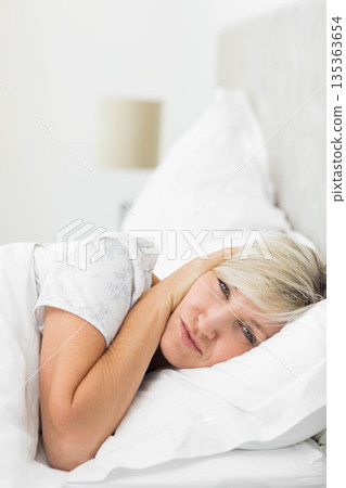 Woman lying on side in bed wearing floral top resting head on pillow next to lamp 135363654
