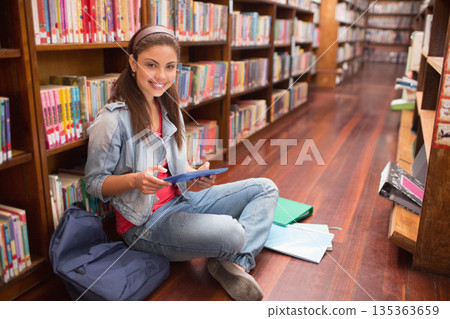 Woman sitting crosslegged at library holding blue tablet near backpack, open notebooks copy space 135363659