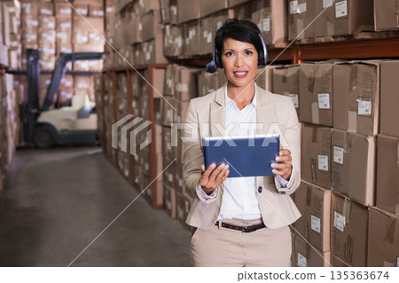 Asian woman in suit using tablet and headset in warehouse with shelves boxes forklift, copy space Asian woman in suit using tablet and headset in warehouse with shelves boxes forklift, copy space 135363674