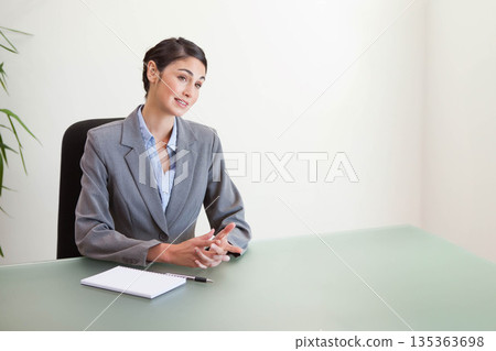 Businesswoman writing on notepad with black pen at conference table near potted plant, copy space Businesswoman writing on notepad with black pen at conference table near potted plant, copy space 135363698