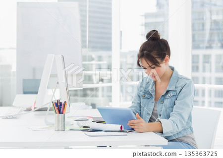 Woman sitting at desk in bright office holding tablet with monitor, keyboard and mouse, copy space 135363725