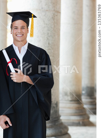 Male graduate standing before stone colonnade in gown holding red ribbon tied diploma, copy space Male graduate standing before stone colonnade in gown holding red ribbon tied diploma, copy space 135363769
