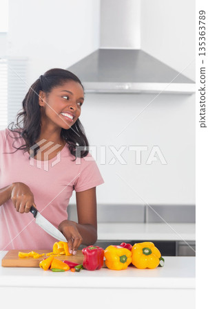 African American woman slicing yellow bell pepper on cutting board using chef's knife in kitchen 135363789