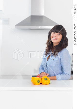 Woman leaning on kitchen island smiling with yellow peppers under range hood, copy space 135363792