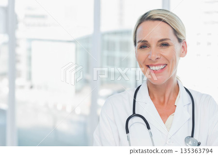 Mature female physician standing at clinic window wearing white lab coat, stethoscope, copy space Mature female physician standing at clinic window wearing white lab coat, stethoscope, copy space 135363794