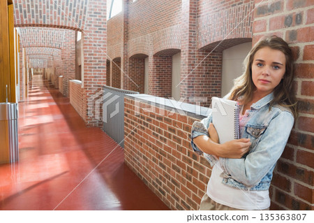 Female student leaning against hallway wall, holding spiral-bound notebooks near railing, trash bin Female student leaning against hallway wall, holding spiral-bound notebooks near railing, trash bin 135363807