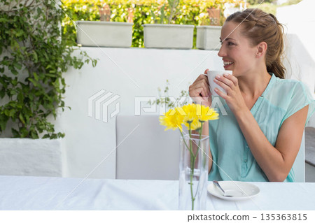 Mid adult woman smiling while holding white ceramic mug on patio with yellow flowers, copy space Mid adult woman smiling while holding white ceramic mug on patio with yellow flowers, copy space 135363815