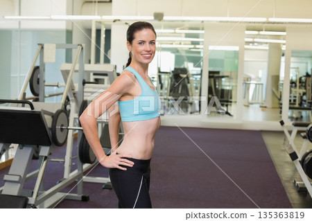 Woman in sportswear standing at gym on purple mat beside bench with barbell plates, copy space Woman in sportswear standing at gym on purple mat beside bench with barbell plates, copy space 135363819