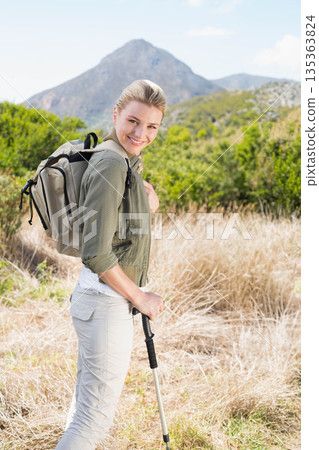 Female hiker wearing jacket standing on mountain slope holding trekking pole and hiking backpack Female hiker wearing jacket standing on mountain slope holding trekking pole and hiking backpack 135363824