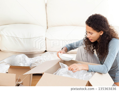 Woman sitting on floor in living room unpacking bowl and bubble wrap from boxes, copy space Woman sitting on floor in living room unpacking bowl and bubble wrap from boxes, copy space 135363836