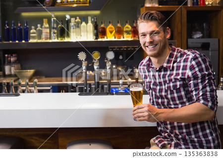 Man sitting at bar counter holding tall beer glass with metal taps, illuminated bottles, copy space Man sitting at bar counter holding tall beer glass with metal taps, illuminated bottles, copy space 135363838