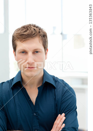 Man standing with crossed arms facing camera in modern office with white window frames Man standing with crossed arms facing camera in modern office with white window frames 135363843