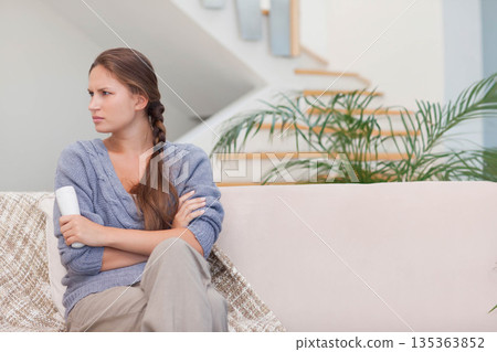 Woman in late twenties holding remote and crossing arms gazing left in living room, copy space Woman in late twenties holding remote and crossing arms gazing left in living room, copy space 135363852