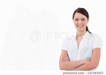 Smiling woman standing with arms crossed facing camera in studio wearing white blouse, copy space 135363857