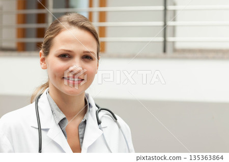 Adult female doctor standing in hospital corridor wearing stethoscope and white coat, copy space 135363864