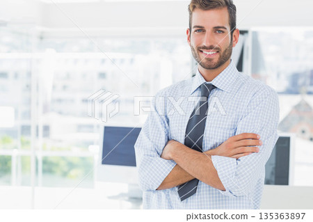Man in checked shirt and tie crossing arms smiling in office near computer monitors, copy space 135363897