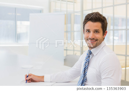 Male professional sitting at desk holding blue pen and reviewing papers in workspace, copy space Male professional sitting at desk holding blue pen and reviewing papers in workspace, copy space 135363903