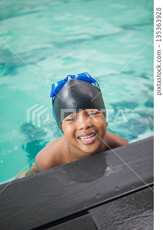 African American child boy leaning on pool deck at turquoise pool wearing black cap, blue goggles African American child boy leaning on pool deck at turquoise pool wearing black cap, blue goggles 135363928