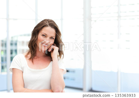 Woman smiling while standing by windows with blinds and blurred building in office wearing t-shirt Woman smiling while standing by windows with blinds and blurred building in office wearing t-shirt 135363933