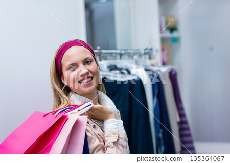 Colorful shopping bags are resting on boutique counter while metal rack is displaying garments Colorful shopping bags are resting on boutique counter while metal rack is displaying garments 135364067