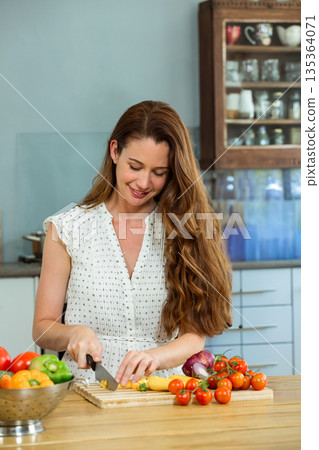Vegetables are being chopped on chopping board at kitchen counter, with bell peppers in colander Vegetables are being chopped on chopping board at kitchen counter, with bell peppers in colander 135364071