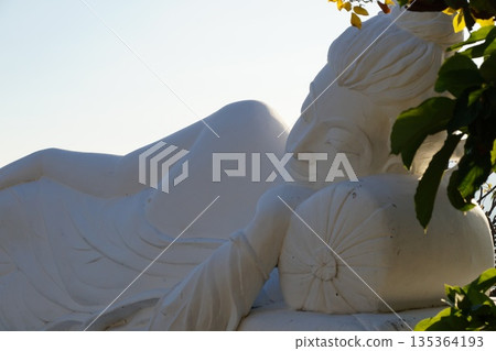 One white Buddha statue lies in a flowering garden. One white Buddha statue lies in a flowering garden. 135364193