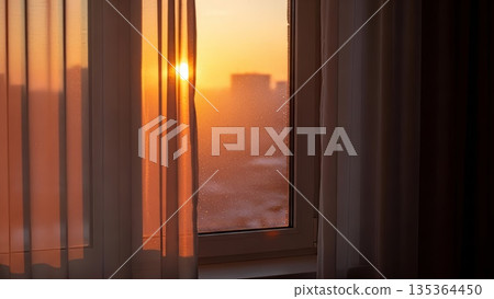 Golden sunset light streaming through window with condensation droplets creating warm orange glow and shadows on interior wall 135364450