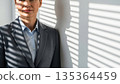 Professional Asian businesswoman in gray suit standing by office window with venetian blind shadows 135364459