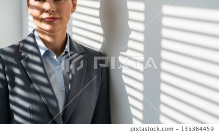 Professional Asian businesswoman in gray suit standing by office window with venetian blind shadows 135364459