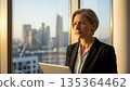 Professional asian businesswoman with laptop looking thoughtfully through office window at city skyline during golden hour 135364462
