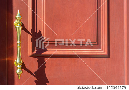 Golden handle casting shadow on red wood door Golden handle casting shadow on red wood door 135364579