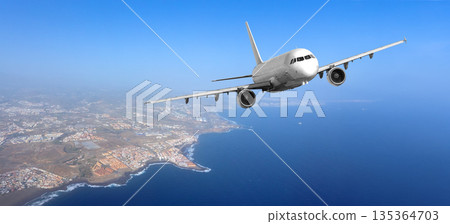 White passenger airplane flying above coastline and ocean 135364703