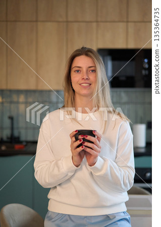 Woman Holding a Warm Cup in a Softly Lit Kitchen Woman Holding a Warm Cup in a Softly Lit Kitchen 135364735