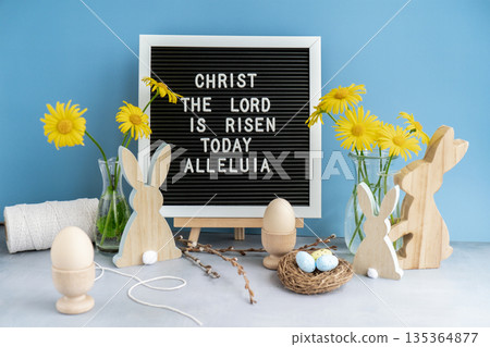 Phrase CHRIST THE LORD IS RISEN TODAY ALLELUIA traditional greeting to christian holiday. Festive mood composition with bunnies and yellow flowers on pastel blue background. Sustainable natural Phrase CHRIST THE LORD IS RISEN TODAY ALLELUIA traditional greeting to christian holiday. Festive mood composition with bunnies and yellow flowers on pastel blue background. Sustainable natural 135364877