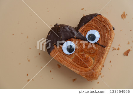 Funny crazy joke eyes on Delicious fresh croissant topped with Dark chocolate flavor Ganache. April fool day concept Creation unique heart shape bakery. Puff pastry holiday love gift present idea Funny crazy joke eyes on Delicious fresh croissant topped with Dark chocolate flavor Ganache. April fool day concept Creation unique heart shape bakery. Puff pastry holiday love gift present idea 135364966
