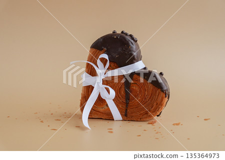 Present gift tied bow holiday Valentine's Day birthday celebration Heart shaped dark chocolate croissant on beige background with copy space. Puff pastry new trendy sweet dessert bakery. Creamy dough 135364973
