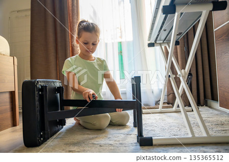Young girl adjusting chair to piano in home interior before music practice. Preparation for lesson, independence, responsibility, and everyday childhood learning routine. Young girl adjusting chair to piano in home interior before music practice. Preparation for lesson, independence, responsibility, and everyday childhood learning routine. 135365512
